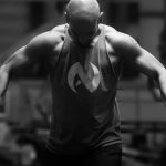 A muscular man works out indoors using gym equipment in dramatic black and white